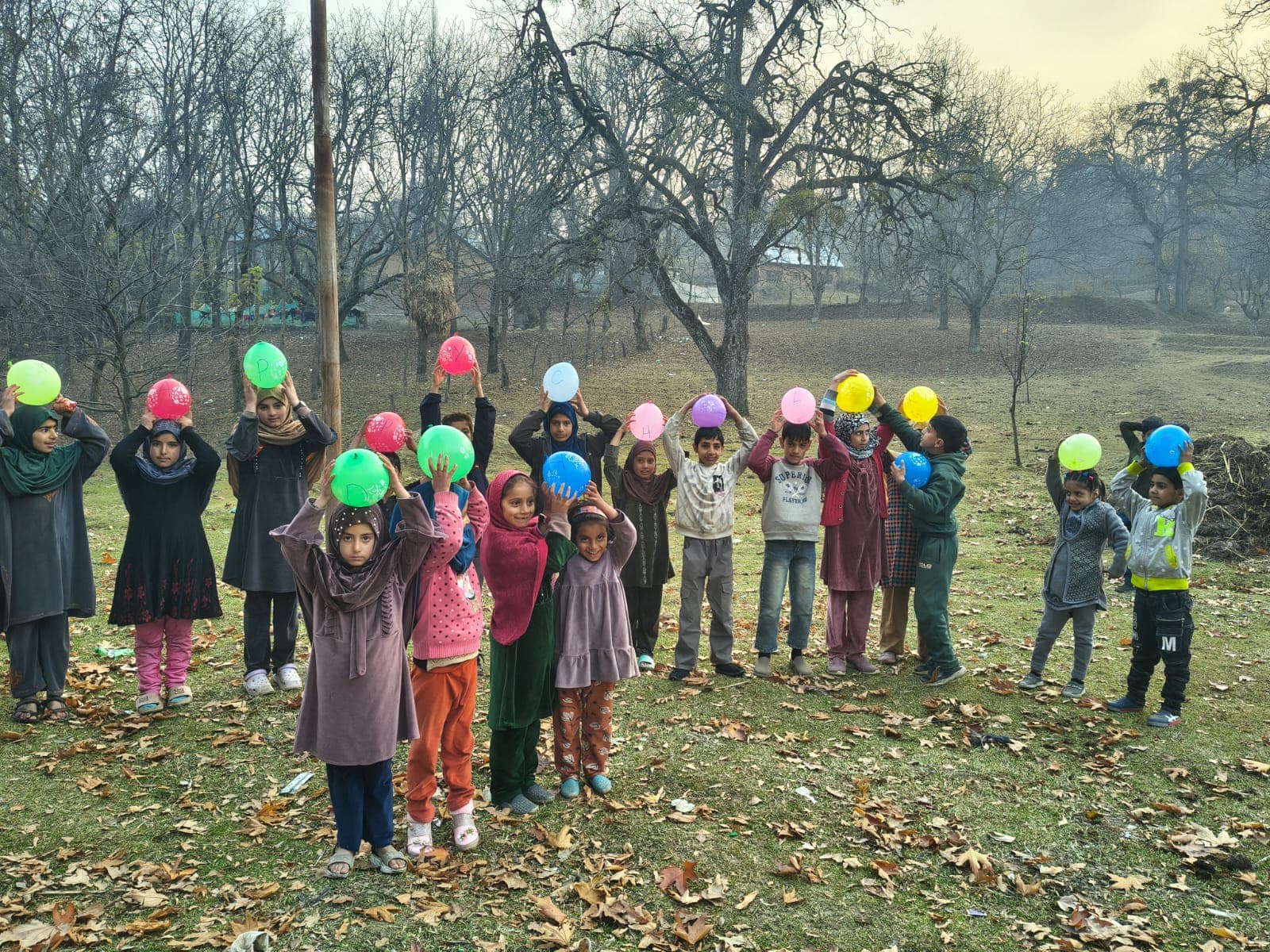 A wide view of children holding lettered balloons in an orchard at dusk