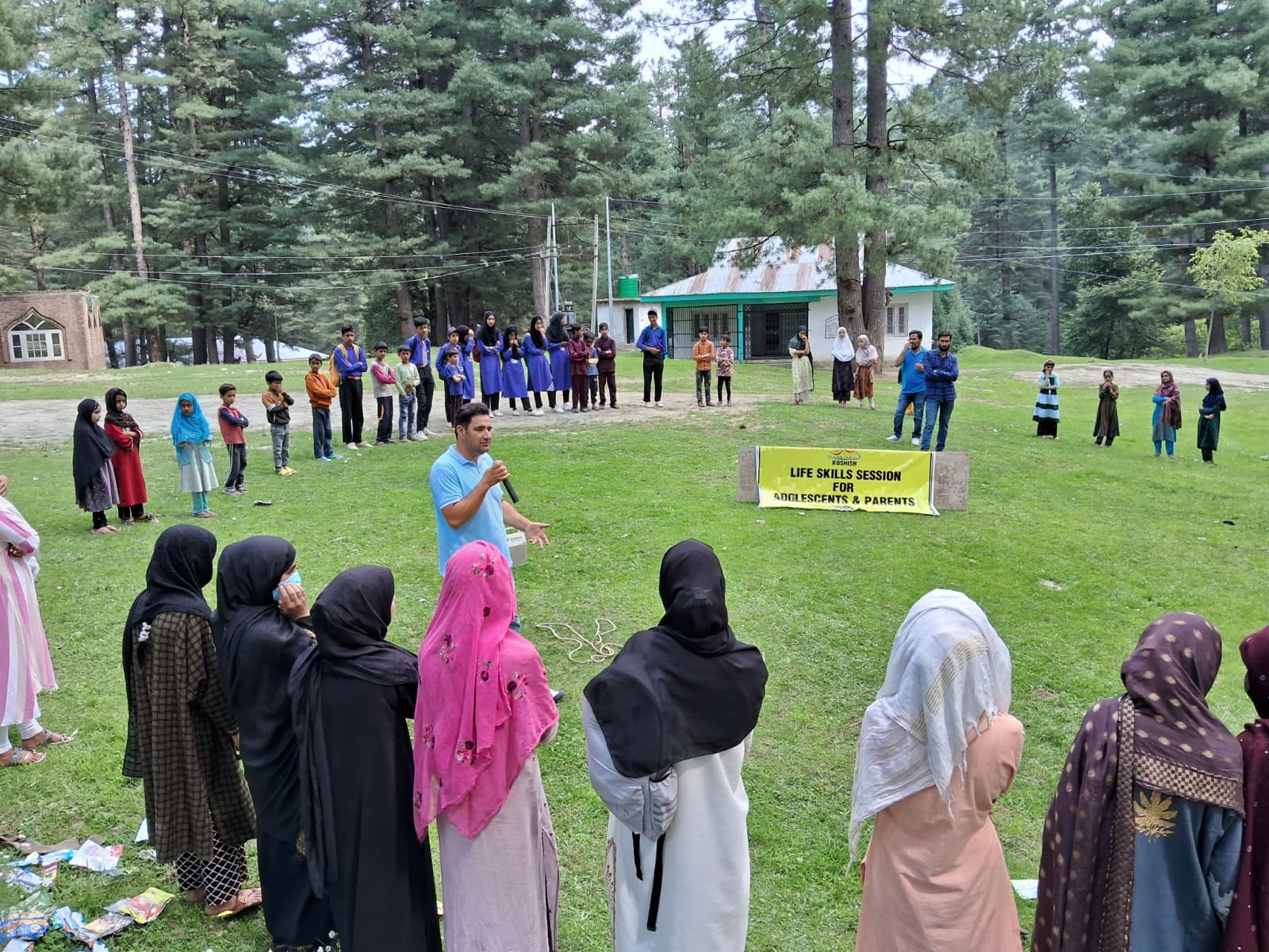 A facilitator speaking into a microphone during a life skills session for adolescents and parents in a park