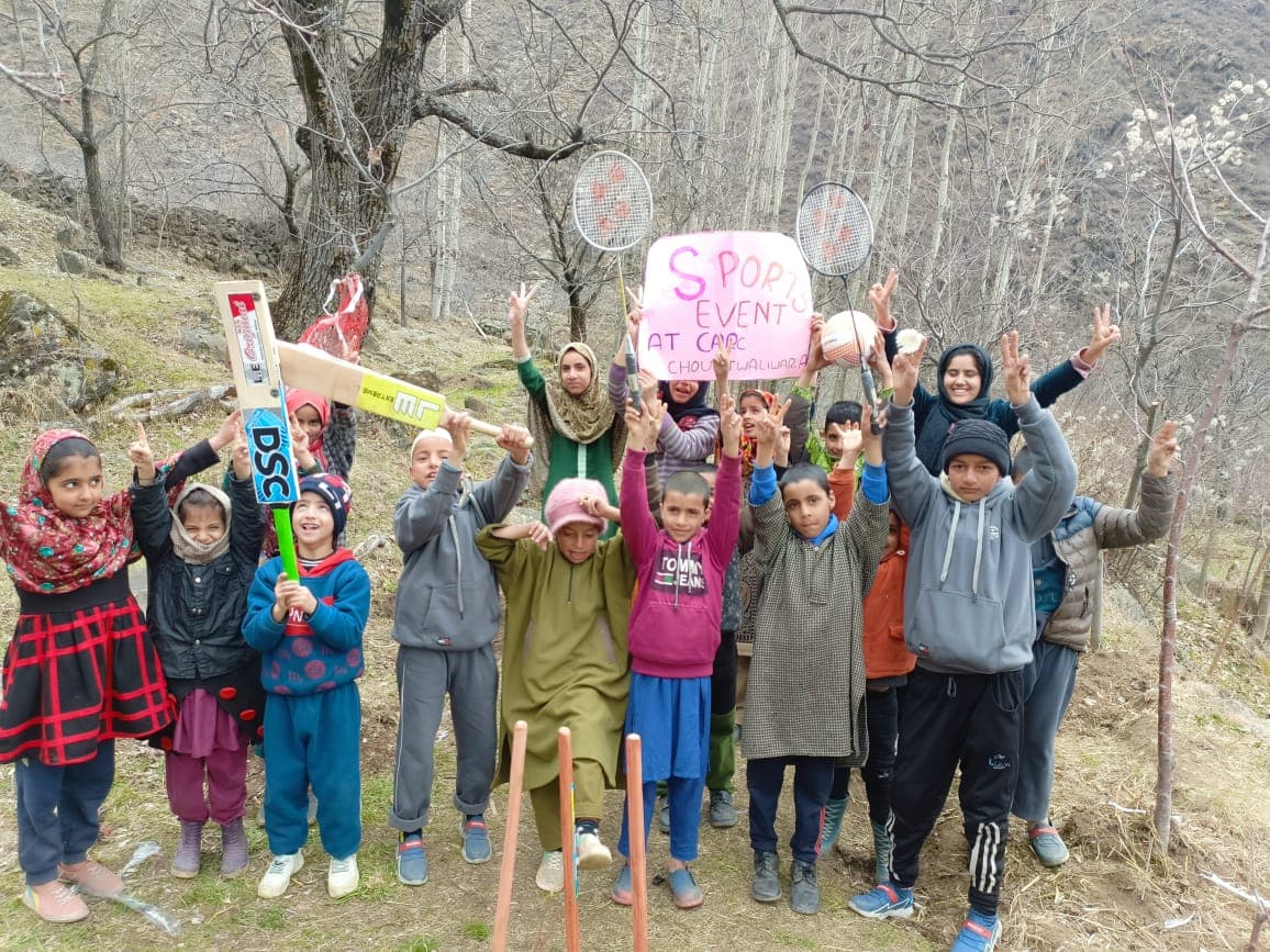 Children cheering and holding cricket bats and badminton rackets at a KOSHISH sports event in the mountains