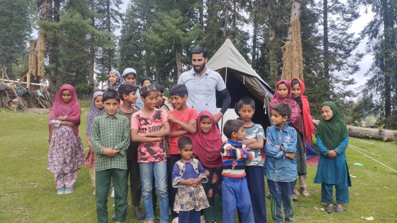 A group of children standing with a KOSHISH facilitator in front of a tent at a highland camp