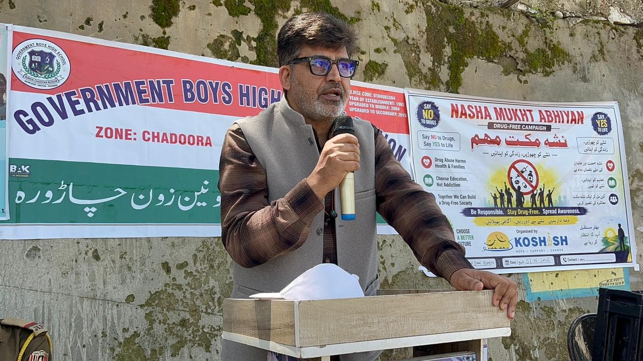 A speaker addressing a gathering at a school beside a KOSHISH drug-free campaign banner