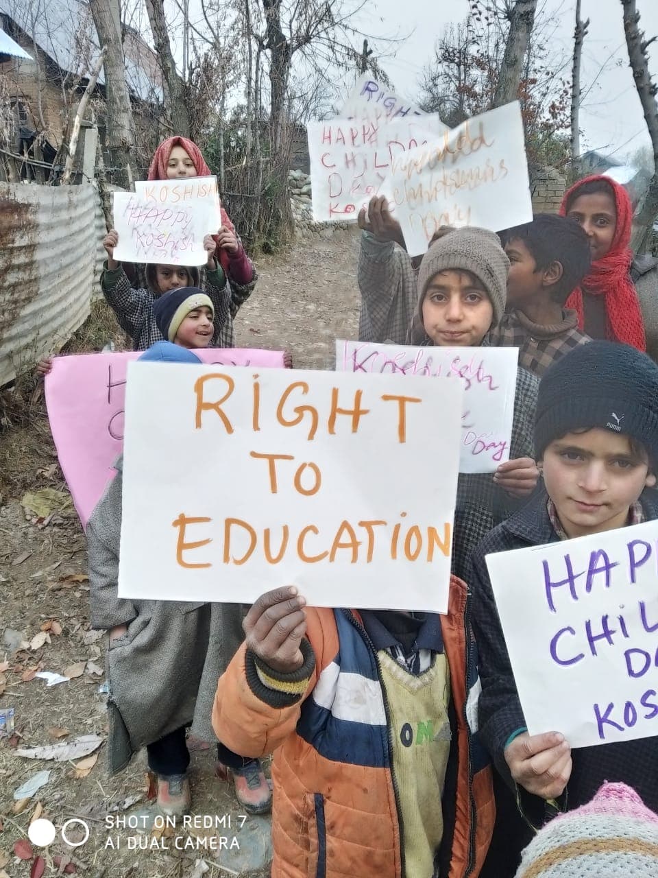Students walking a village road behind a banner for a Government Girls Middle School enrolment drive